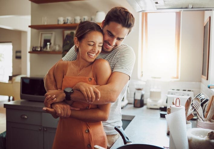 Young couple sharing a cuddle, while cooking on the stove in the kitchen.
