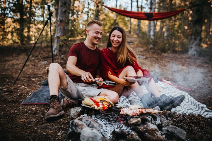 Couple preparing food on a campfire.