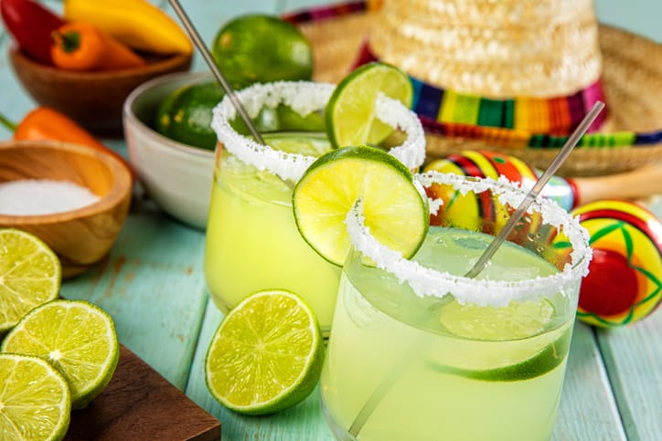 Margarita glasses with a rim of salt surrounded by fresh cut limes.