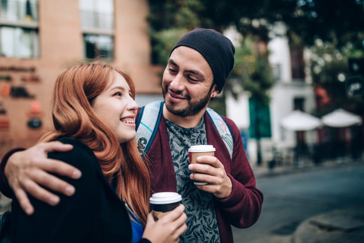 man with arm around woman's shoulder walking