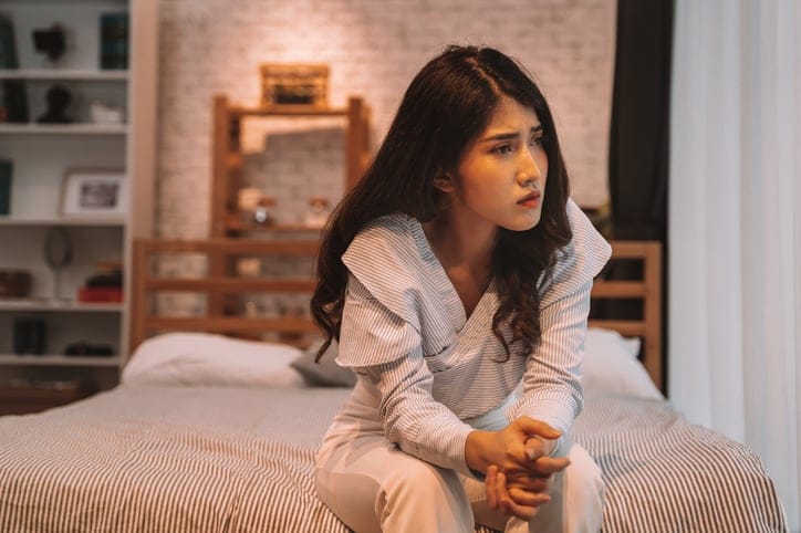 Scared woman sitting on bed.