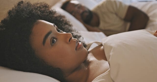 Woman laying awake next to her boyfriend.