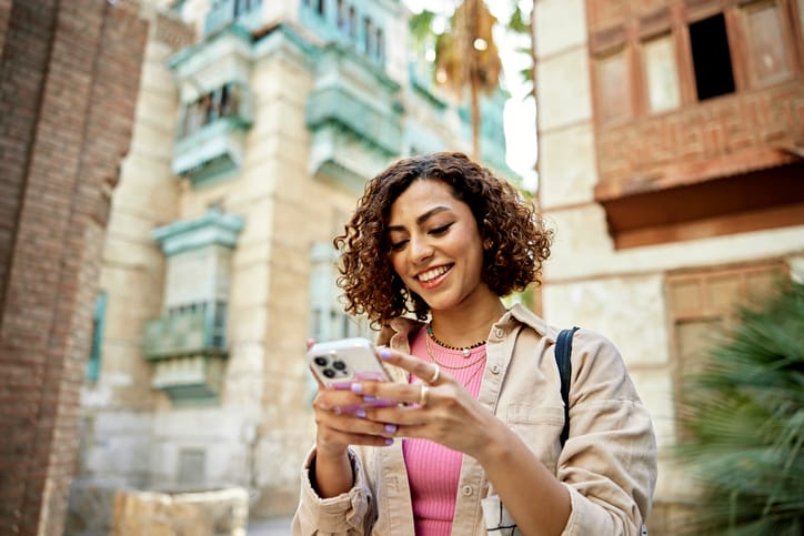 Woman smiling and texting in a Middle Eastern city.
