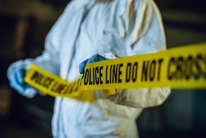 Forensic detective with crime tape at a scene.