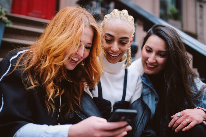 3 female friends reading text nyc brownstone stoop