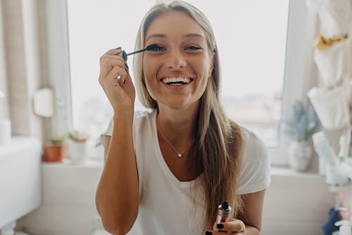 Young woman is smiling while putting on her mascara.