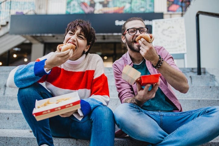 Couple eating hot dogs outdoors.