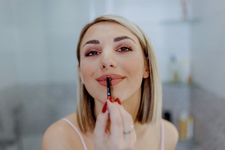 Woman applying lipstick in bathroom mirror.