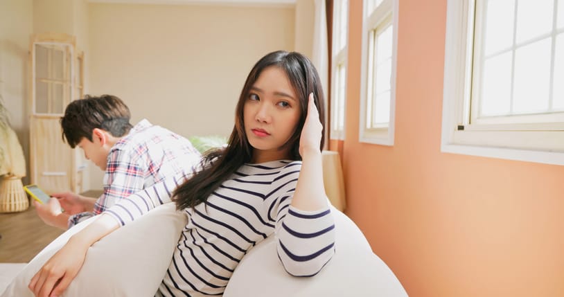 upset woman on couch while boyfriend texts