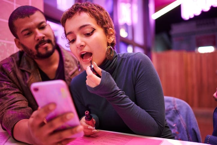 Woman applying lipstick at a restaurant.
