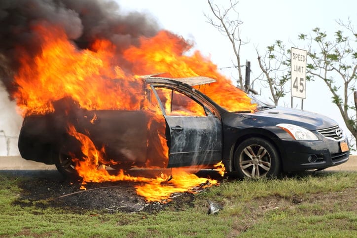 Car on fire on side of highway.