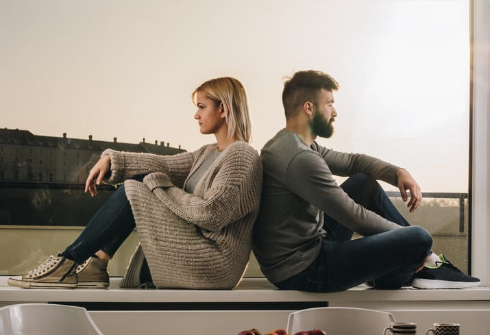 Sad couple ignoring each other while sitting back to back on a window sill.