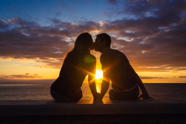Man and woman sitting by the sea at sunset.