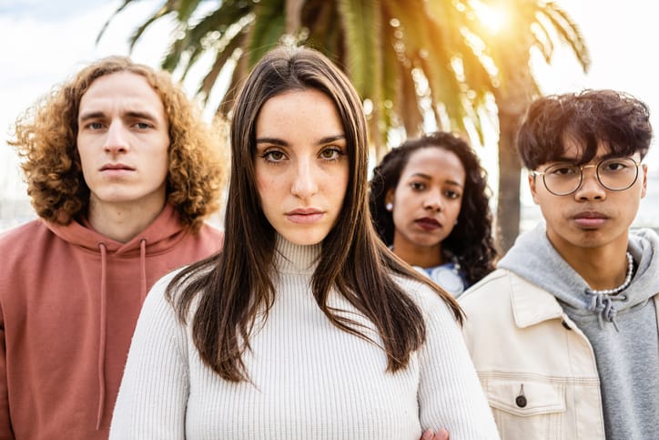 Portrait of unhappy millennial group of young people - United serious millennial student friends standing in street looking serious at camera