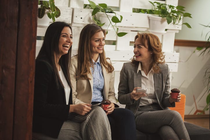 Three female colleagues are on a break from work, eating muffins and chatting.