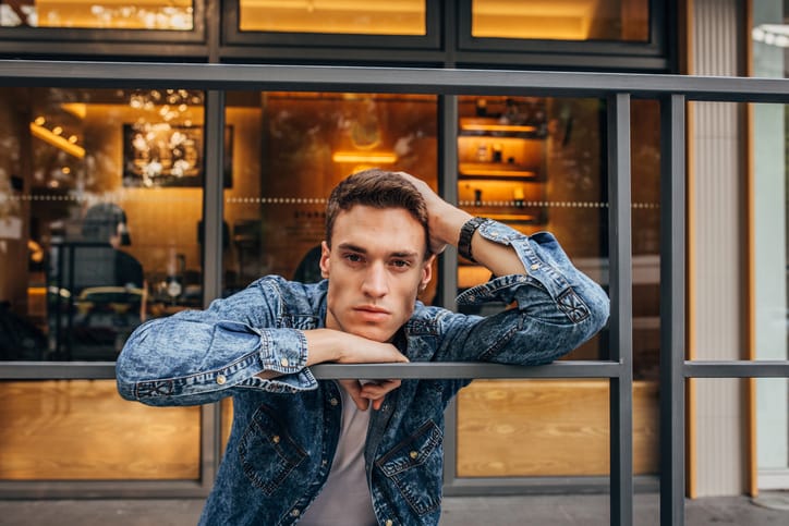 Handsome young man in denim shirt standing outdoors.