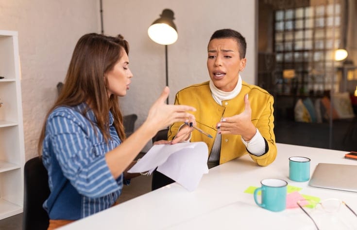 two colleagues gossiping at work desk