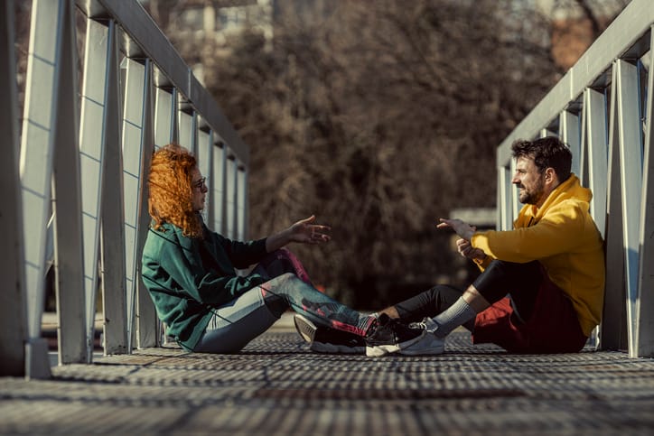 The girl explains to her friend what stretching exercises she wants to do while sitting on the footbridge and resting.