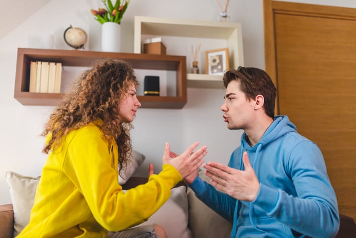 A beautiful young heterosexual couple arguing passionately in the living room. They are having a fight.