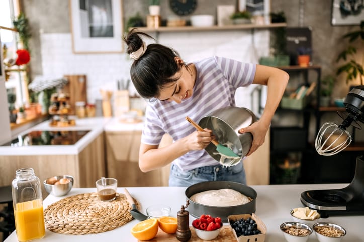 Woman pouring cheesecake filling into baking tin,