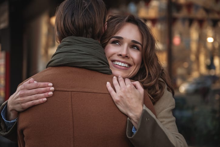 Portrait of happy young woman cuddling man with love. She is looking up dreamingly and laughing