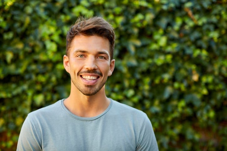 smiling man outdoors in front of greenery