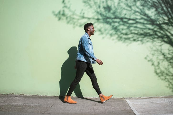 A young adult enjoys the sunshine as he strolls down a city walkway.