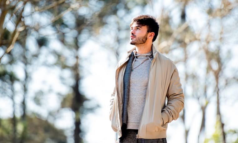 Pensive young man looking off in the distance while out for a walk alone in a park in spring