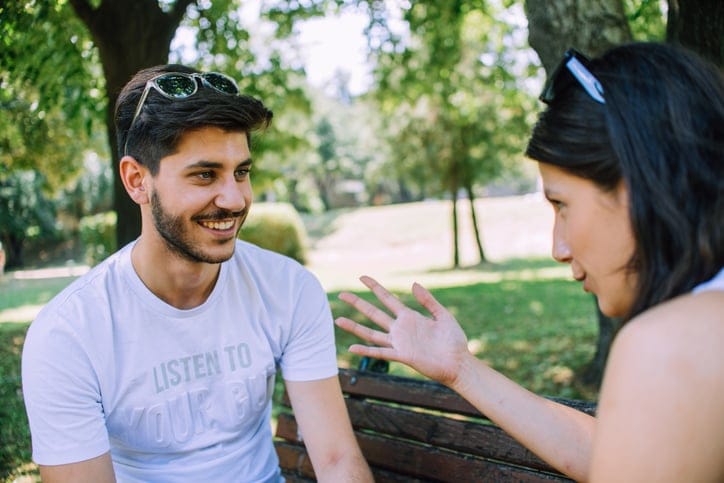 Male and female friend chatting on park bench.
