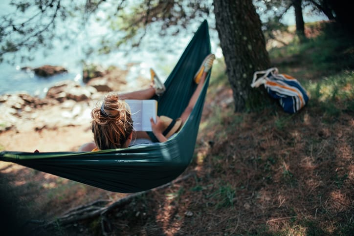 A young woman is reading a book while relaxing in a hammock.