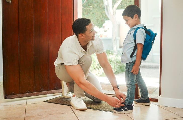 Little boy carrying a backpack and getting help from his parent.