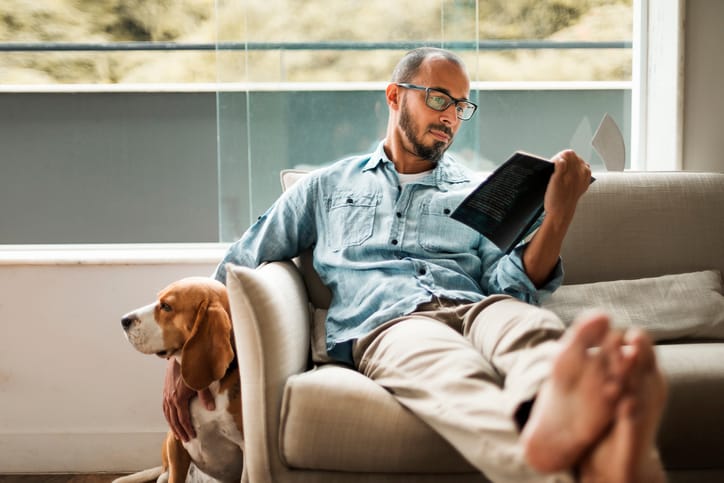 Man comfortably sitting on a coach reading a book.