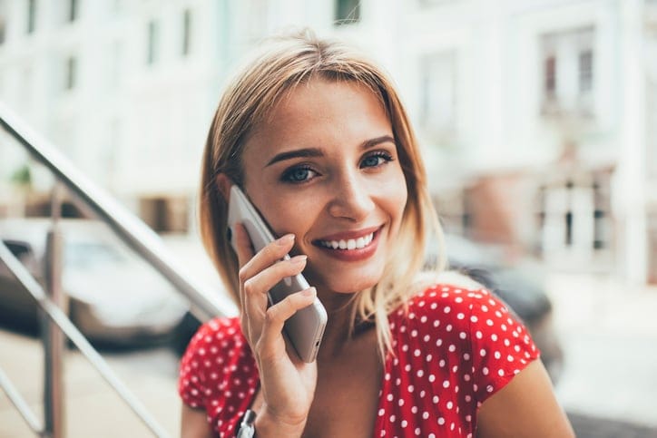 Smiling woman on phone outside.
