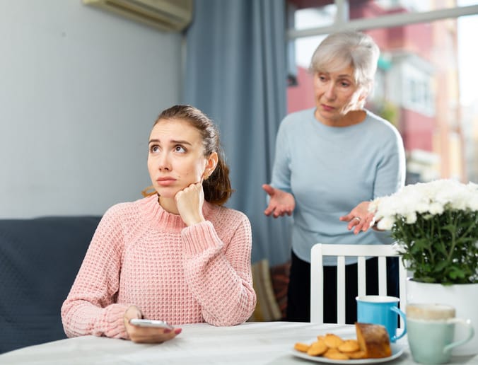 Woman sitting at table with her mother standing beside.