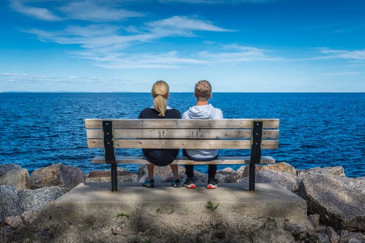 People relaxing on a bench by a lake.