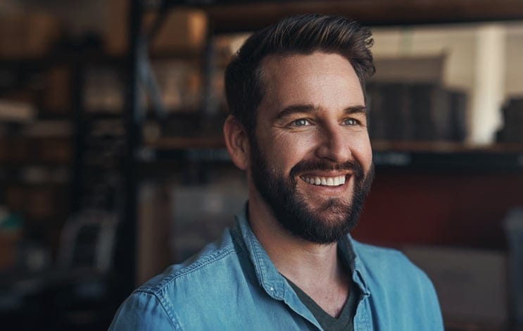 Happy, smile and young man in a studio with positive, good and confident attitude for small business. Happiness, pride and male person from Canada with entrepreneurship mindset in a modern office.