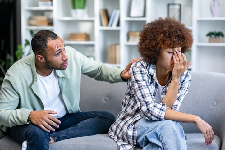 A couple sitting on a couch in the living room, woman seems upset and man trying to calm woman