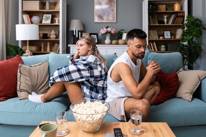 Stressed young married couple sitting separately on different sides of sofa ignoring each other.