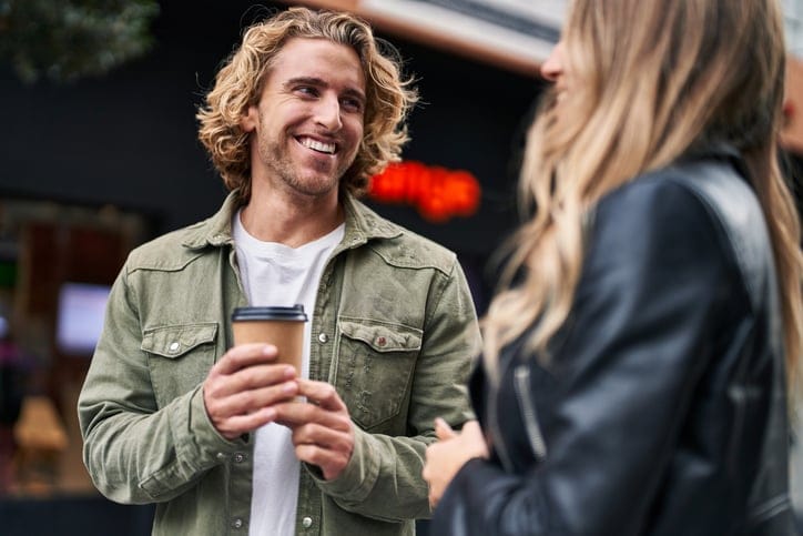 Man and woman smiling and drinking coffee on the street.