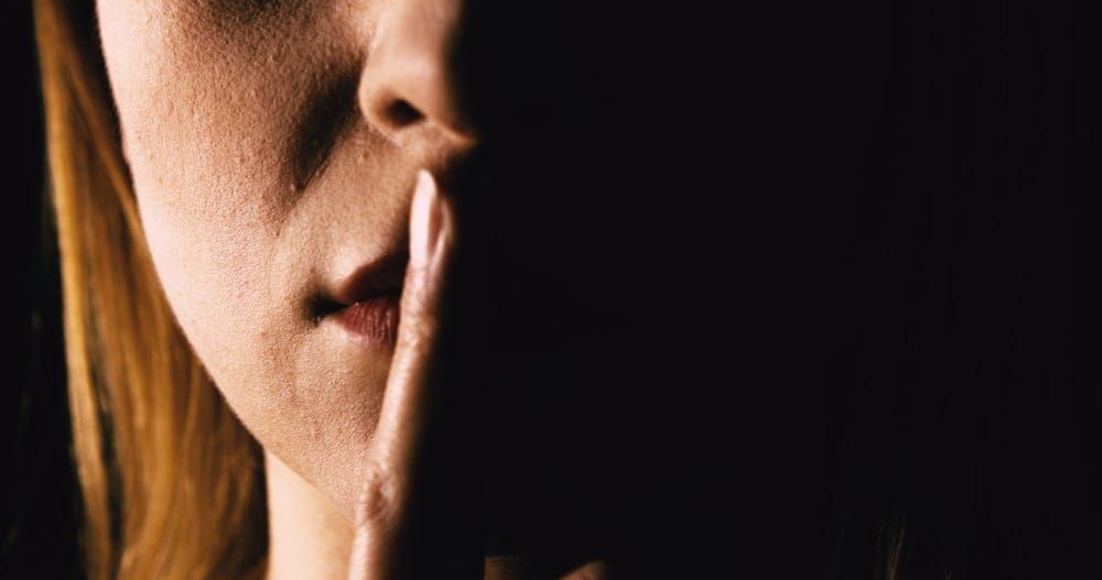 Woman places her finger over her mouth in silence.