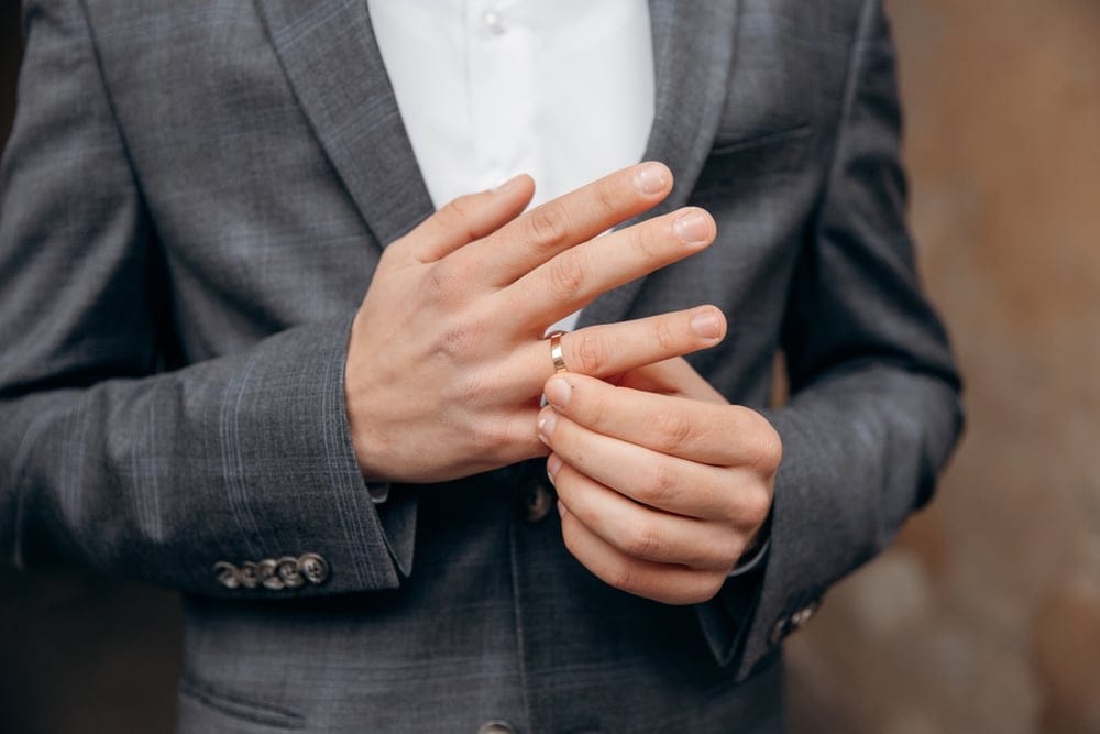 Man in gray suit jacket removing wedding ring.