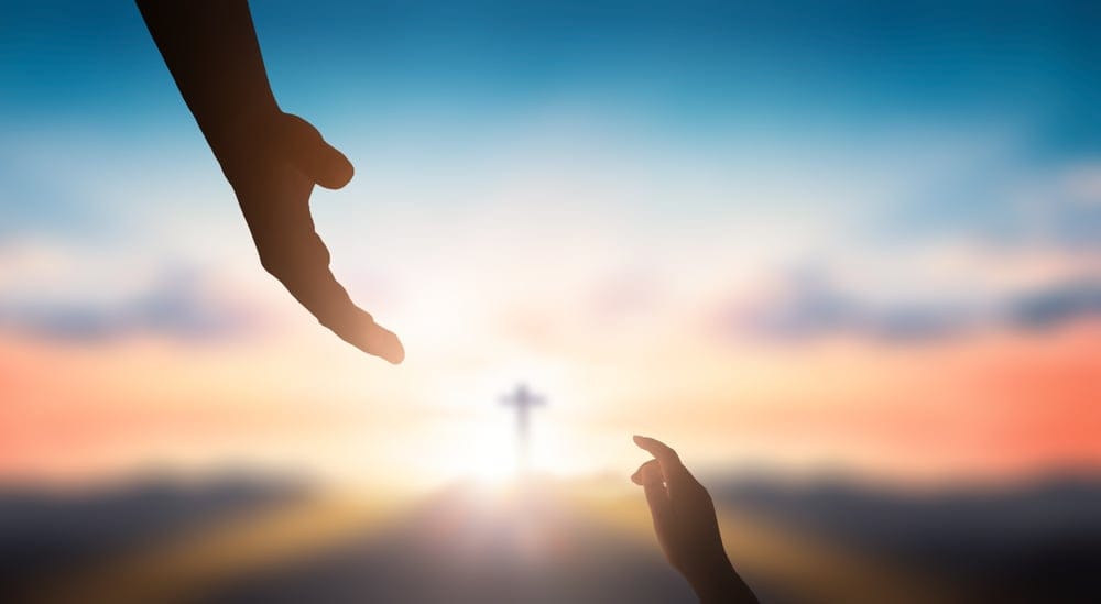 Two hands and a cross in the distance.