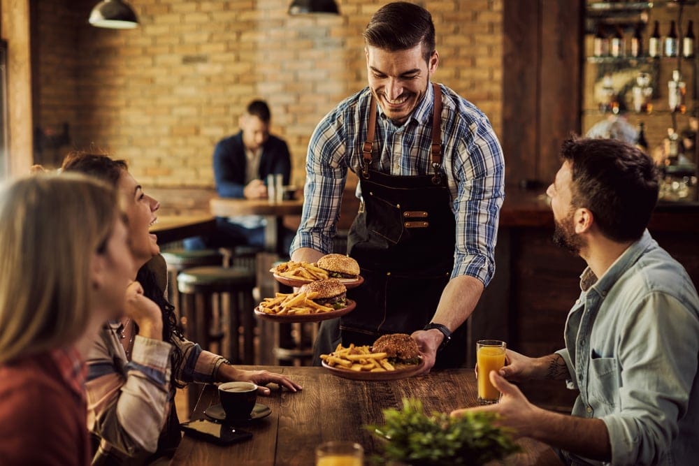 A restaurant waiter with food at the table.