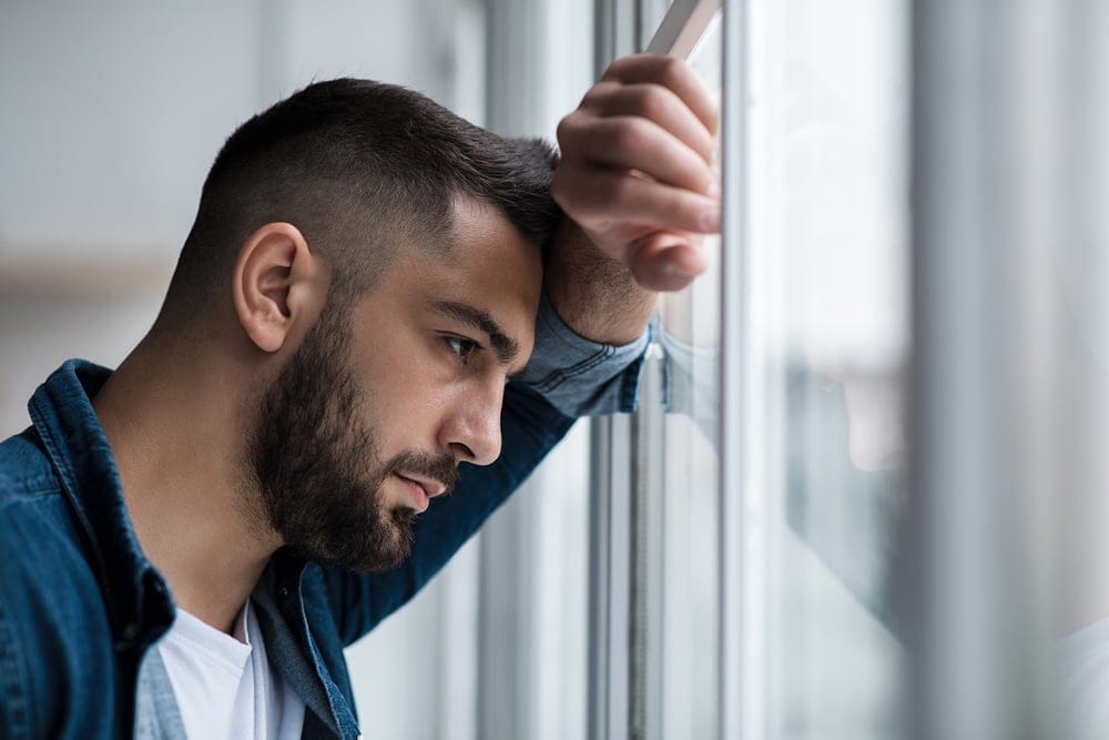 A man looking out the window in sadness.