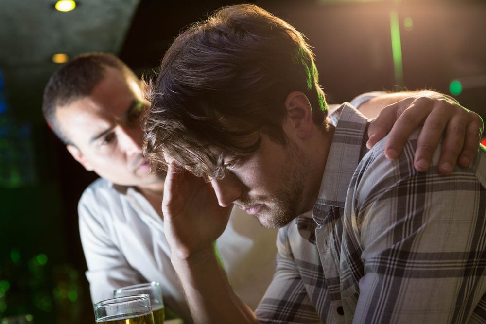 A young man comforting his male friend at a bar at night