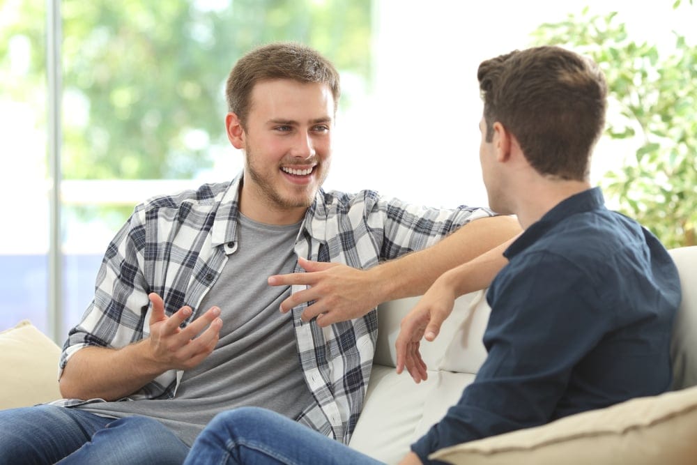 Two male friends sitting together talking.