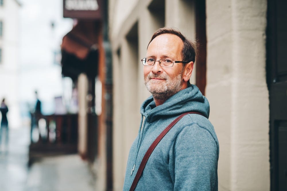 A man wearing a blue sweater on a walk outside.