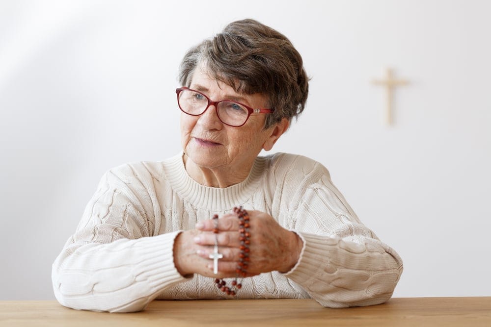 Older woman praying with rosary beads.