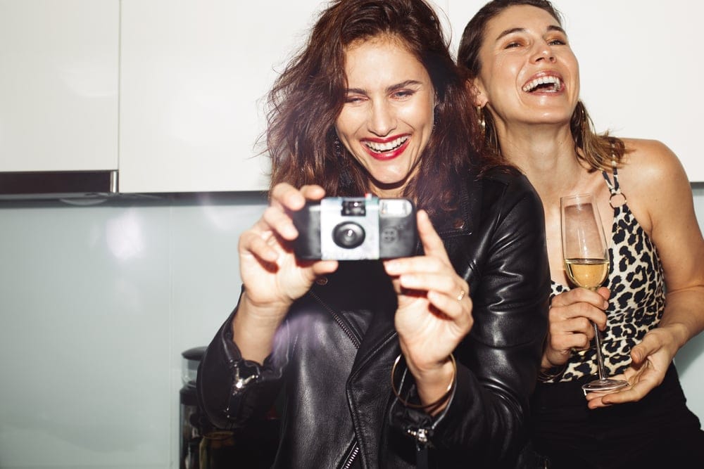 Two women smiling and taking photographs.