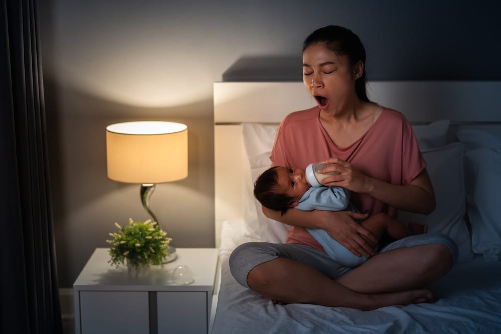 Sleepy Mother Yawning And Feeding Milk To Newborn Her Baby.
